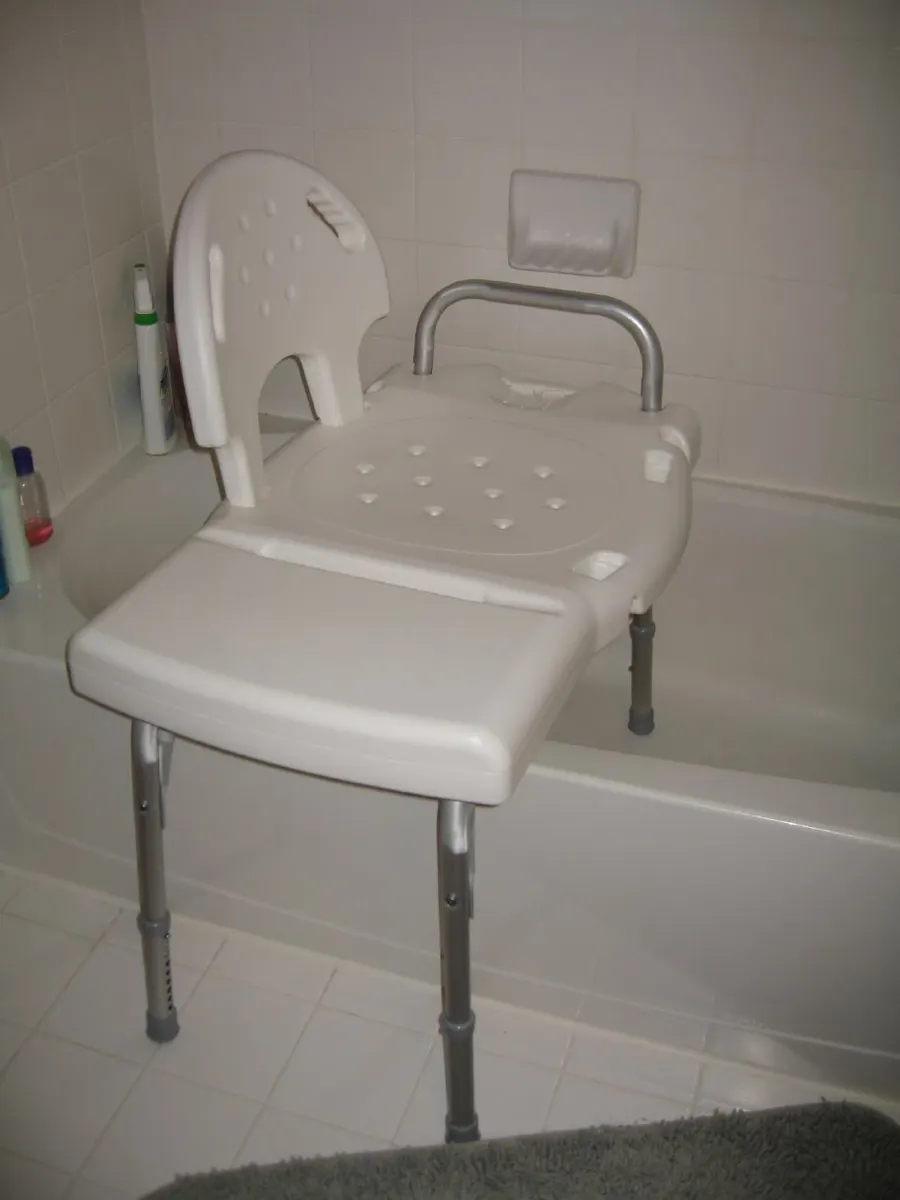 A plastic tub transfer bench with a backrest and handle, its legs straddling the side of a bathtub.