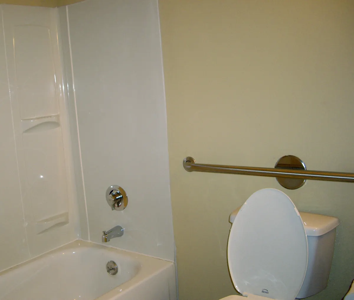 A home bathroom with a horizontal metal grab bar mounted on the wall between a bathtub and a toilet.