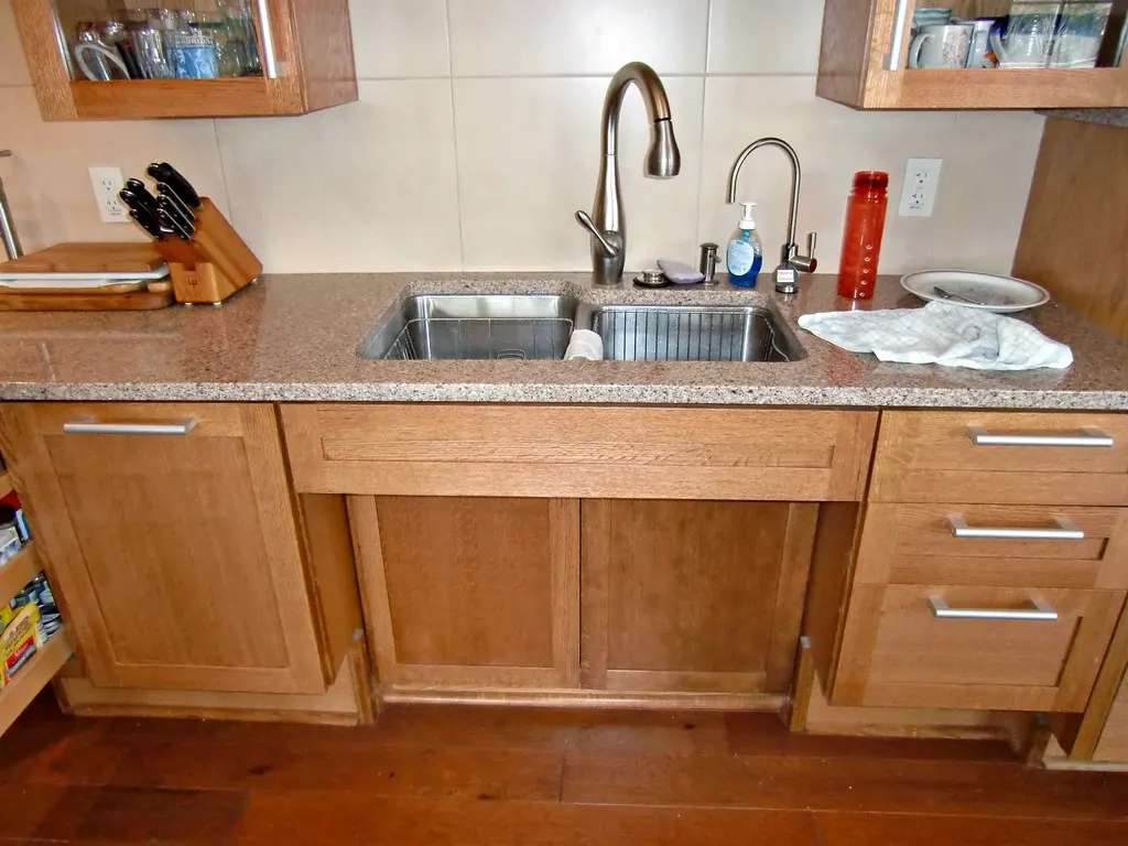 A kitchen sink in a granite counter with the cabinet below removed to leave open knee space, between two banks of drawers.