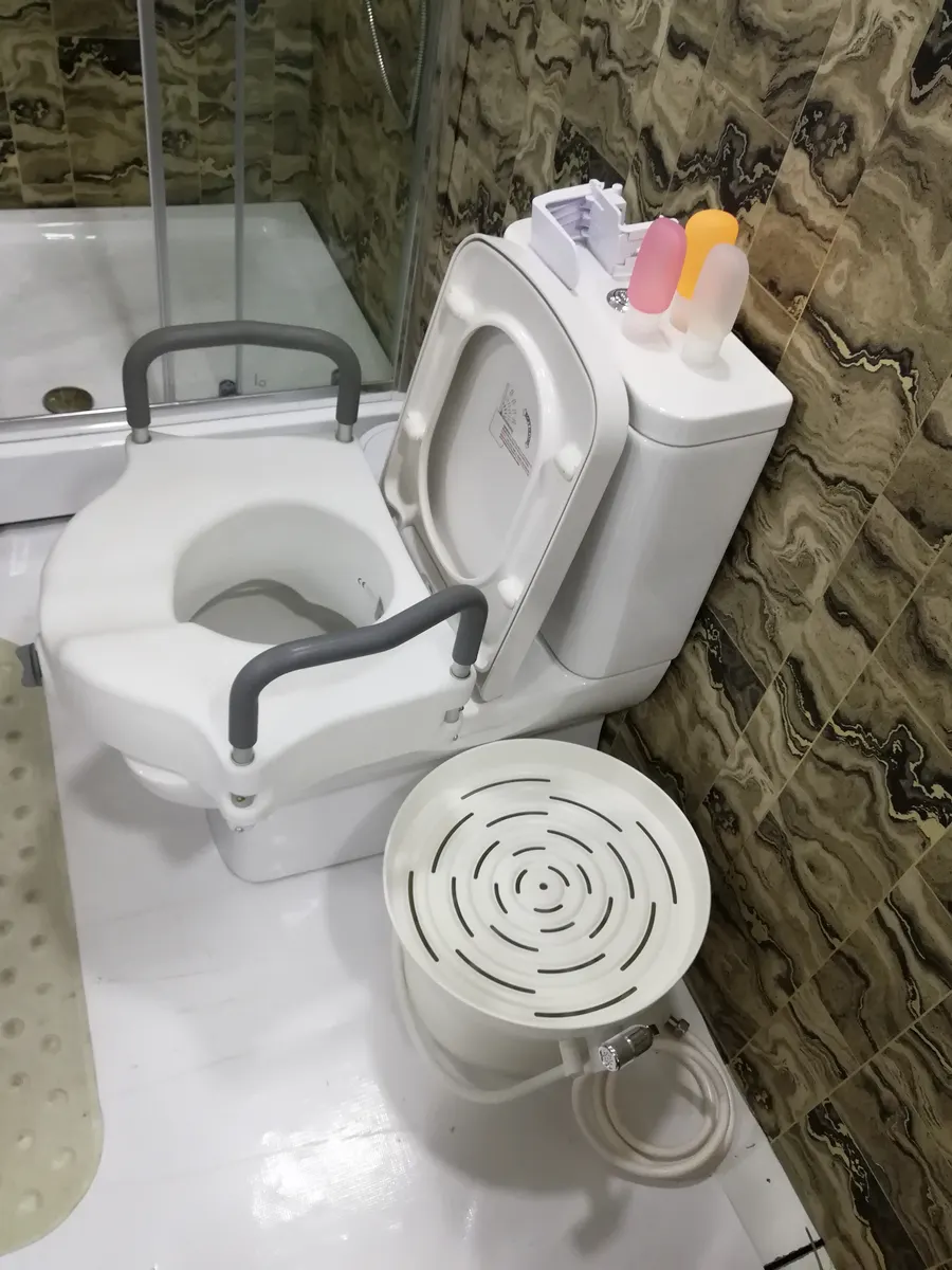 A white raised toilet seat with grey padded armrests fitted onto a toilet.
