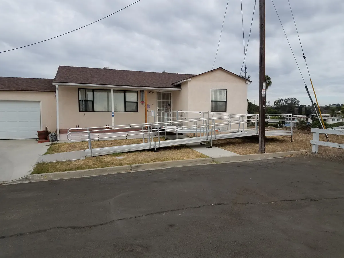 A modular metal ramp with handrails running along the front of a single-storey house to its entrance.