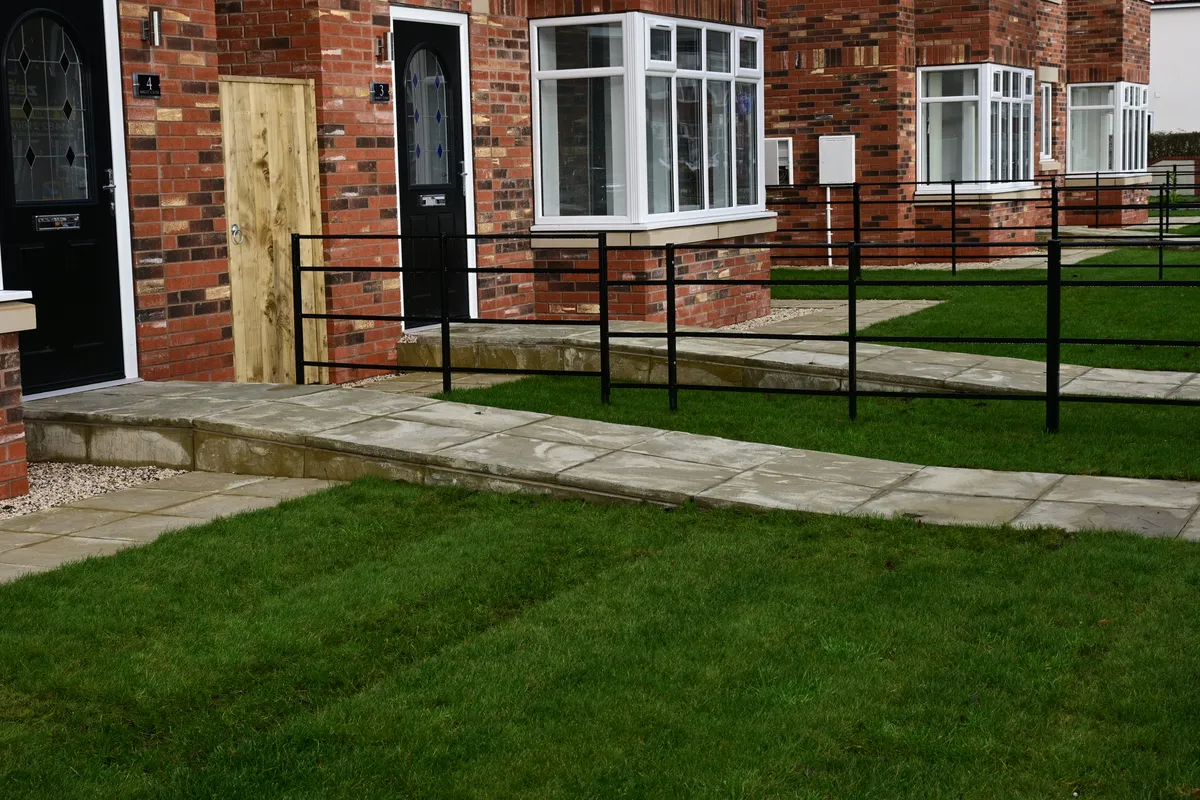 Two gently sloping paved ramps with black steel rails leading across front lawns to the doors of new brick houses.