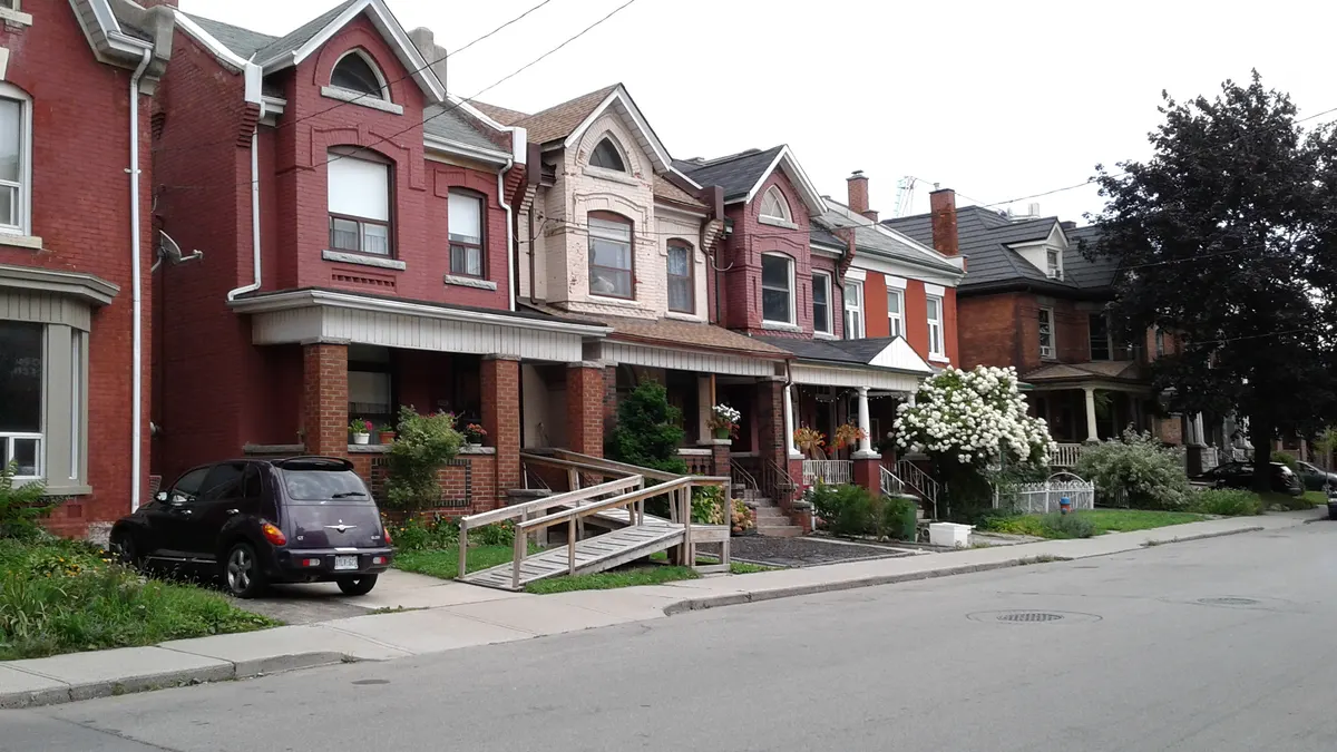 A wooden ramp with handrails leading to the porch of a brick row house in Hamilton, Ontario.
