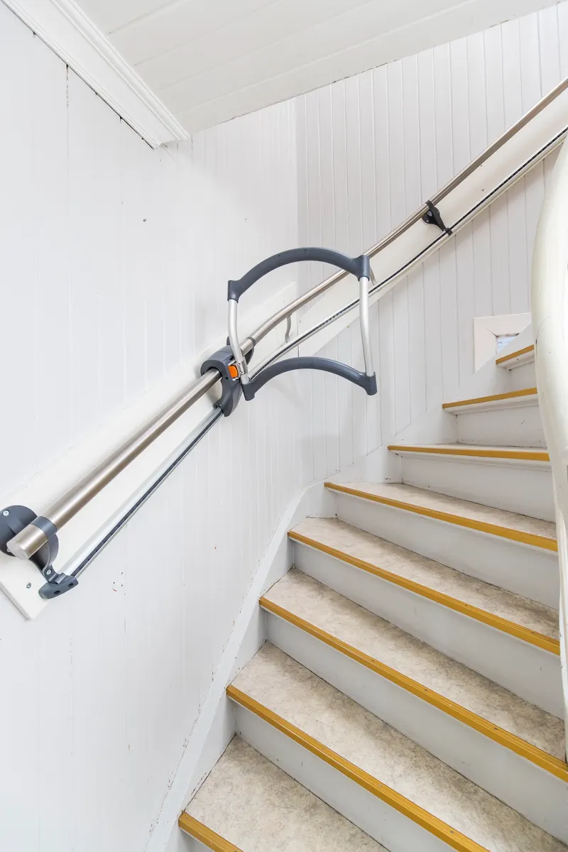 A handrail running up a narrow white staircase, with a sliding assist handle attached to the rail.